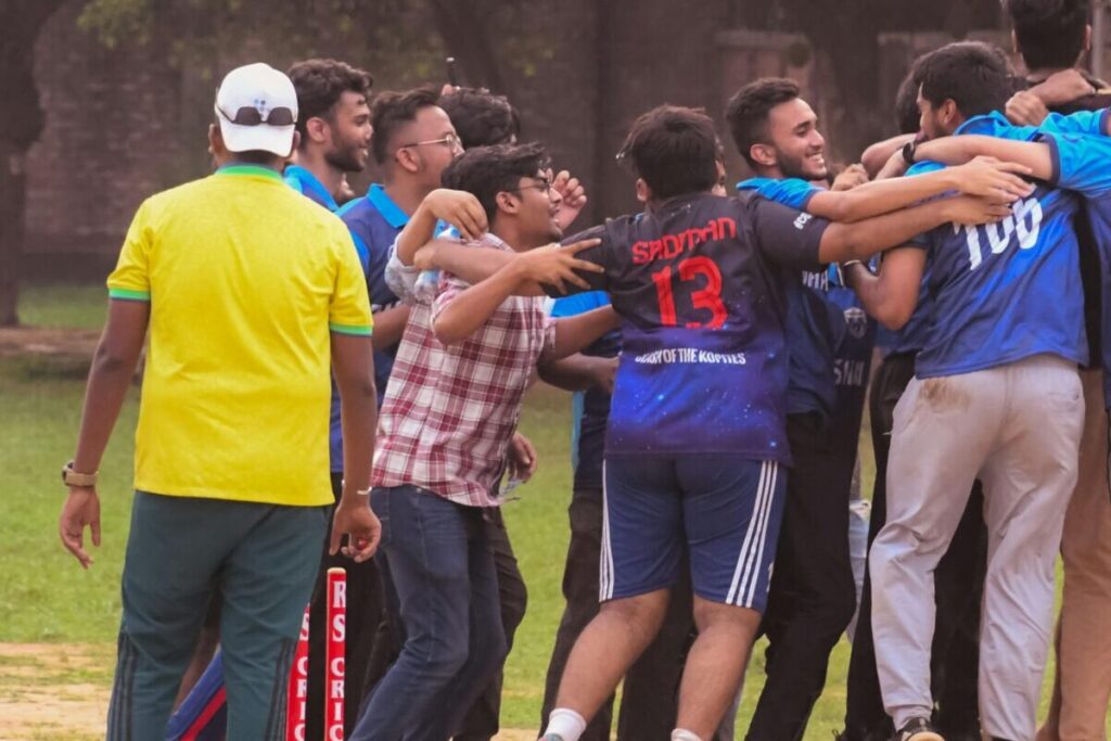 Excited group of male cricket players celebrate a win on a sports field outdoors.